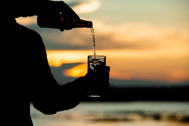 silhouette d'homme tenant une bière pendant un coucher de soleil