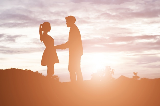 Silhouette de jeune couple tenant les mains avec coucher de soleil de montagne ba