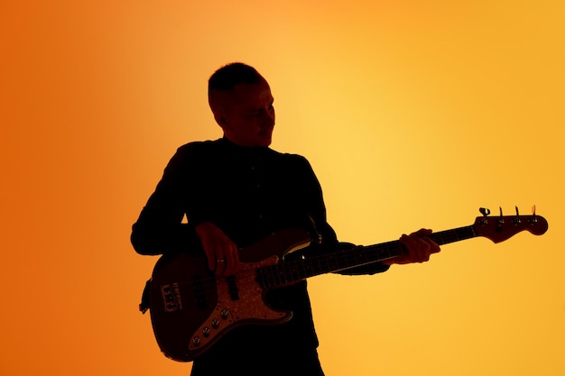 Silhouette de jeune guitariste masculin caucasien isolé sur un studio dégradé bleu-rose en lumière néon
