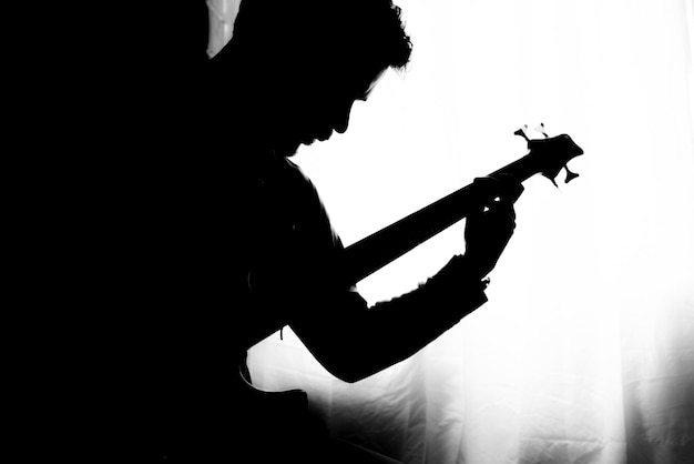 Silhouette d'un jeune homme jouant de la guitare basse électrique