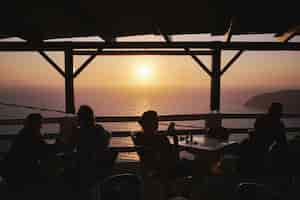 Photo gratuite silhouette de personnes profitant de leur temps au coucher du soleil dans un café à la plage de potamos, grèce