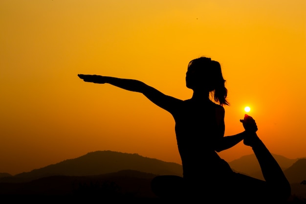 Silhouette - Yoga girl s'exerce sur le toit pendant le coucher du soleil.