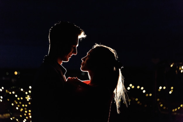 Silhouettes d&#39;un charmant jeune couple debout sur le toit dans la nuit