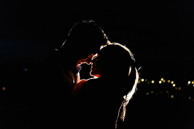 Silhouettes d&#39;un charmant jeune couple debout sur le toit dans la nuit