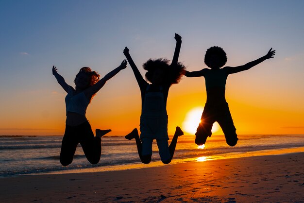 Silhouettes complètes de personnes sautant au coucher du soleil