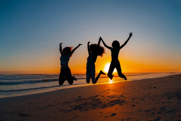 Silhouettes complètes de personnes sautant au coucher du soleil