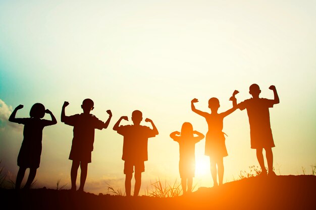 Les silhouettes des enfants montrant les muscles au coucher du soleil