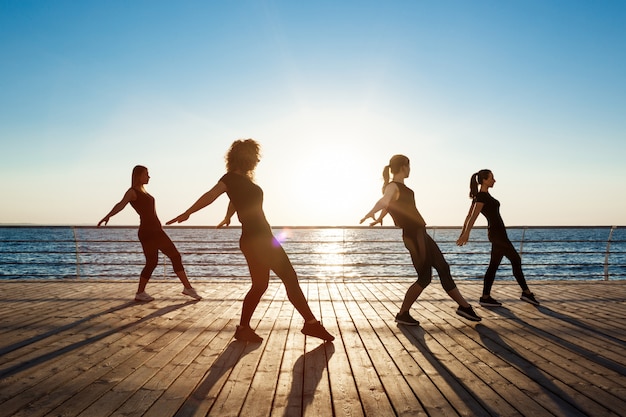 Silhouettes de femmes sportives dansant près de la mer au lever du soleil