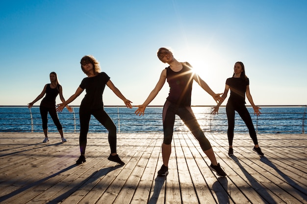 Photo gratuite silhouettes de femmes sportives dansant près de la mer au lever du soleil