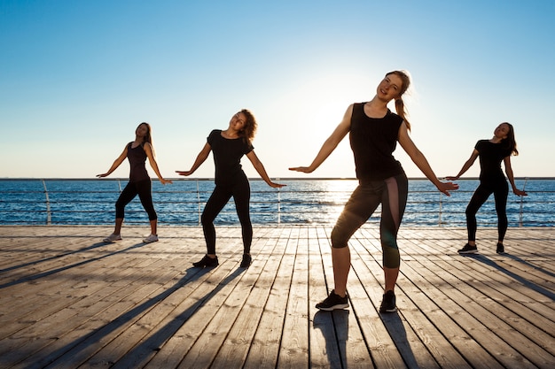 Silhouettes de femmes sportives dansant la zumba près de la mer au lever du soleil