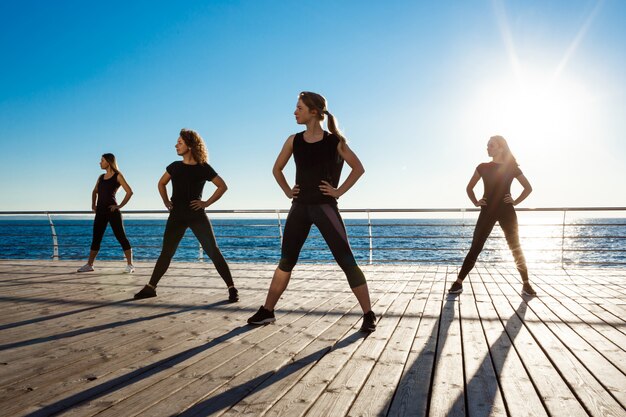 Silhouettes de femmes sportives dansant la zumba près de la mer au lever du soleil