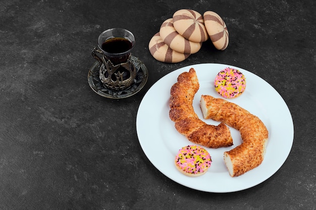 Simit, biscuits feuilletés, biscuits au cacao et un verre de thé sur table noire.