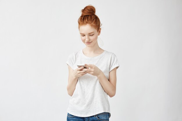 Sincère femme rousse souriante regardant téléphone.