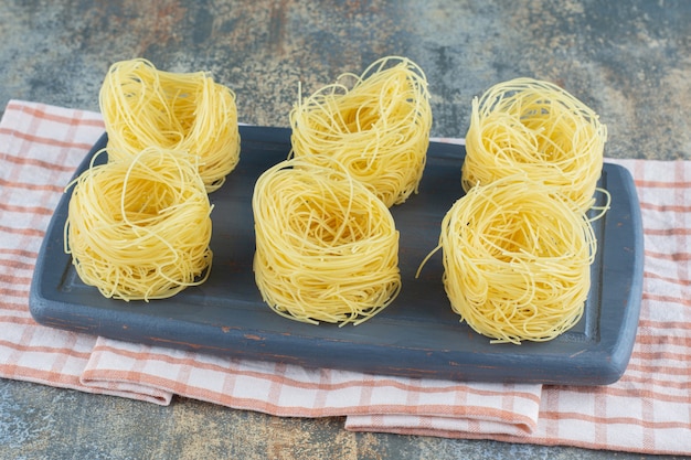 Six piles de spaghettis minces dans le tableau, sur une serviette, sur la surface en marbre.