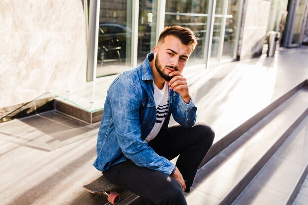 Skateboarder masculin contemplé, assis sur une planche à roulettes