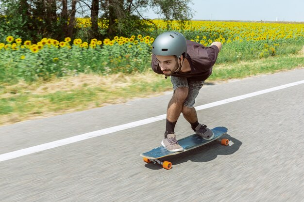 Skateur faisant un tour dans la rue de la ville en journée ensoleillée. Jeune homme en équipement d'équitation et de longboard en action. Concept d'activité de loisirs, sport, extrême, passe-temps et mouvement. Aussi rapide qu'une voiture.