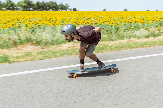 Skateur faisant un tour dans la rue de la ville en journée ensoleillée. Jeune homme en équipement d'équitation et de longboard en action. Concept d'activité de loisirs, sport, extrême, passe-temps et mouvement. Aussi rapide qu'une voiture.