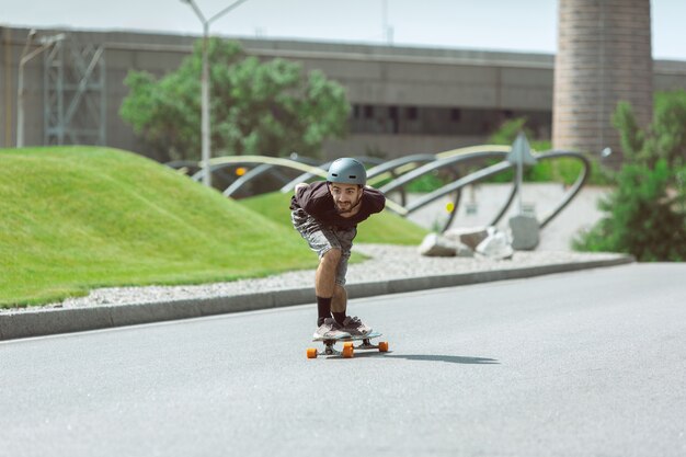 Skateur faisant un tour dans la rue de la ville en journée ensoleillée. Jeune homme en équipement d'équitation et de longboard sur l'asphalte en action. Concept d'activité de loisirs, sport, extrême, passe-temps et mouvement.