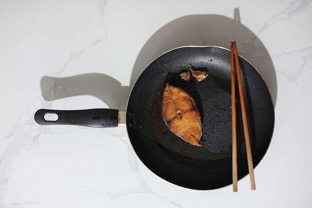 Skillet avec du poisson cuit et baguettes