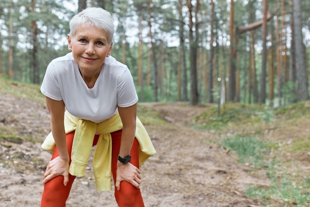 Slim femme d'âge moyen sportive en vêtements de sport debout sur fond de pins se penchant en avant