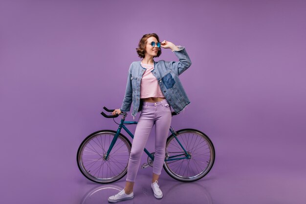 Slim femme blithesome posant avec vélo. Plan en intérieur d'un modèle féminin bouclé en pantalon violet.