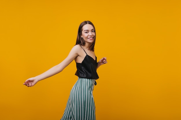 Slim femme brune en élégante danse débardeur noir. magnifique fille aux cheveux bruns s'amusant avec un intérieur lumineux.