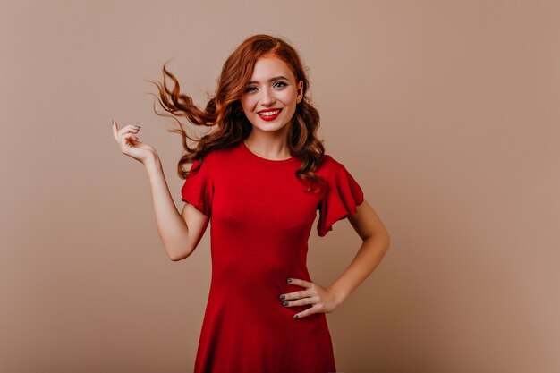 Slim femme caucasienne en robe rouge en riant. Superbe fille au gingembre jouant avec ses cheveux pendant la séance photo.