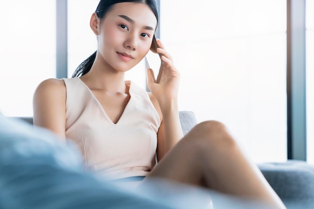 Smart attrayant belle femme asiatique travaillant à la maison main utiliser smartphone s'asseoir dans le canapé sosfa fond intérieur de la maison se détendre et sentir l'expression de travail décontractée