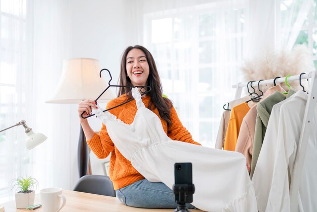 Smart attrayant souriant femme asiatique propriétaire d'entreprise entrepreneur main tenir une tasse de café portrait tourné en regardant la caméra avec une femme confiante assise sur une table au home studio