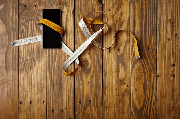 Smartphone attaché au mètre de couture présenté sur la vue de dessus de table en bois rustique