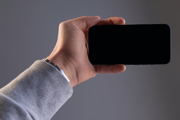 Smartphone moderne rectangulaire noir dans une main masculine sur un fond gris isolé téléphone horizontalement