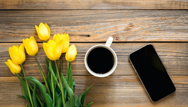 Smartphone une tasse de café un bouquet de tulipes jaunes sur un fond en bois