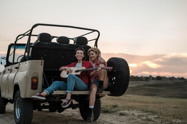 Smiley amies voyageant en voiture et jouant de la guitare