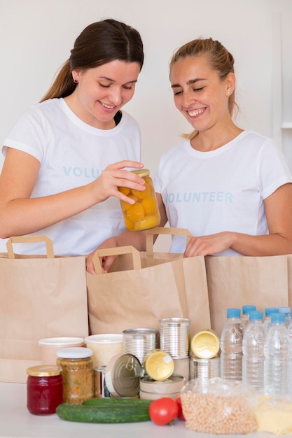 Photo gratuite smiley bénévoles avec des sacs de nourriture et d'eau pour un don