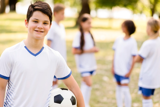 Photo gratuite smiley boy tenant un ballon de football à côté de ses coéquipiers