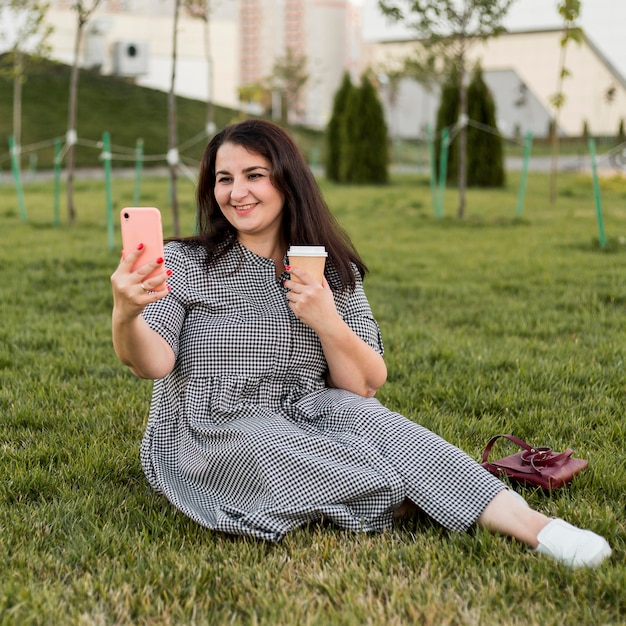 Smiley brunette woman prenant un selfie tout en tenant son téléphone