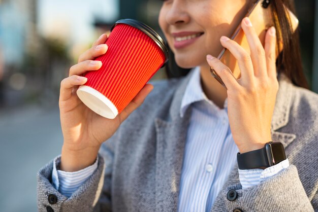 Smiley businesswoman parler au téléphone tout en prenant un café à l'extérieur