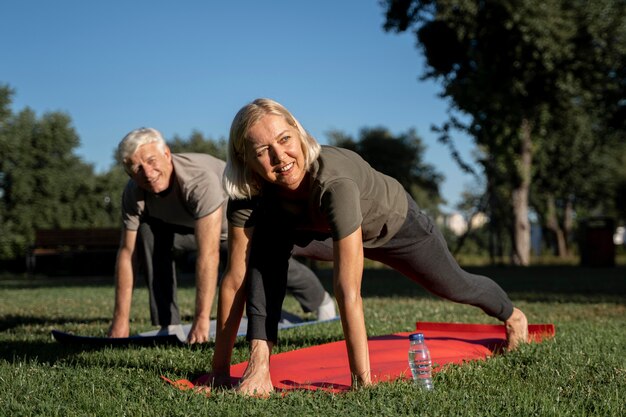 Smiley couple de personnes âgées pratiquant le yoga en plein air