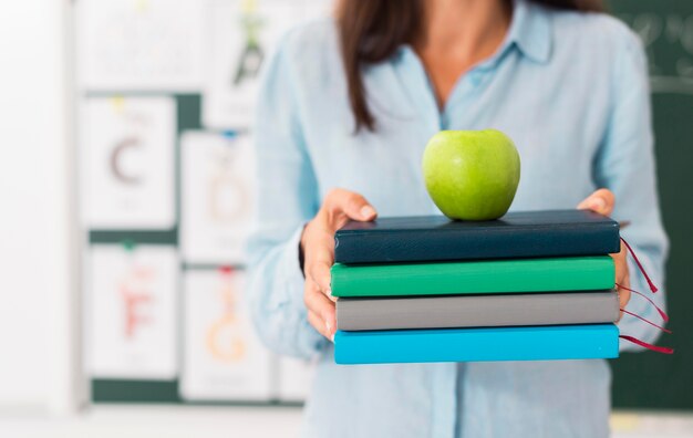 Smiley enseignant tenant un tas de livres et une pomme