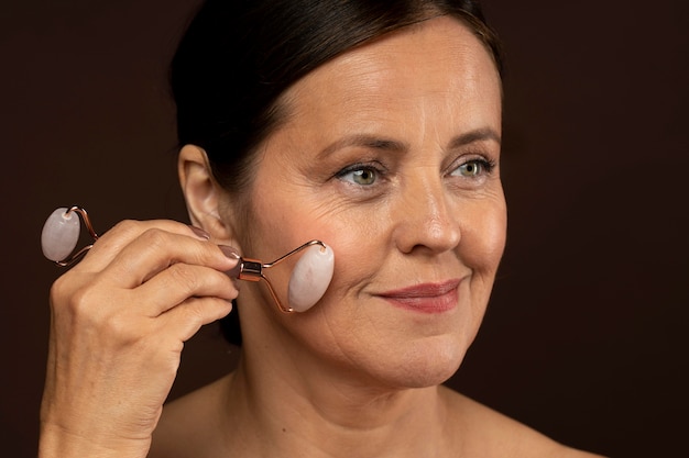 Smiley femme âgée à l'aide d'un rouleau de quartz rose sur son visage