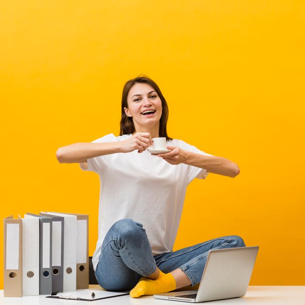 Smiley femme assise sur le bureau et profiter de sa tasse de café