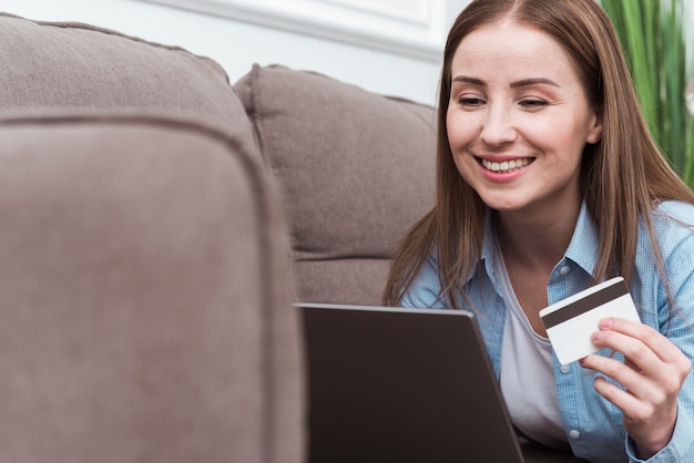 Smiley femme assise sur un canapé et tenant une carte de crédit