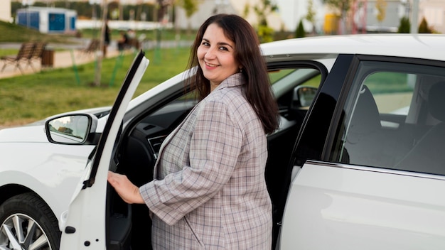 Smiley femme brune debout à côté de la voiture blanche