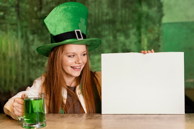 Photo gratuite smiley femme célébrant st. patrick's day au bar avec pancarte vierge et boisson