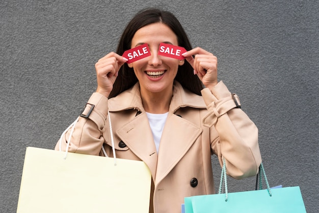 Photo gratuite smiley femme couvrant ses yeux avec des étiquettes de vente tout en tenant des sacs à provisions