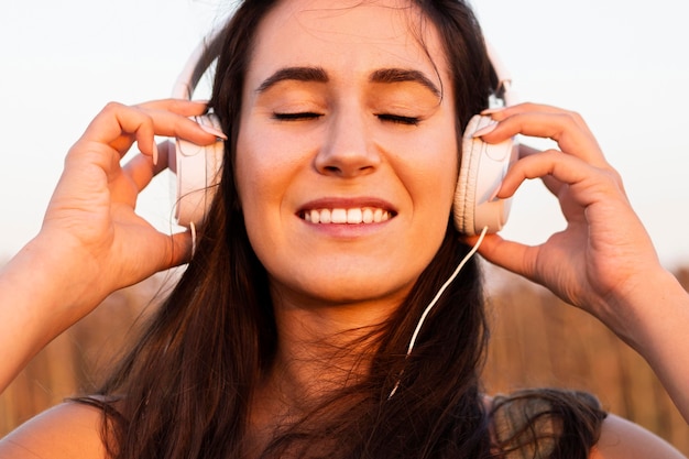 Smiley femme écoutant de la musique à l'extérieur au soleil