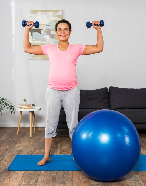 Smiley femme enceinte exerçant à la maison avec des poids et balle