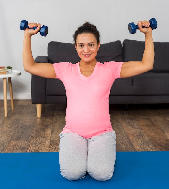 Photo gratuite smiley femme enceinte exerçant avec des poids à la maison