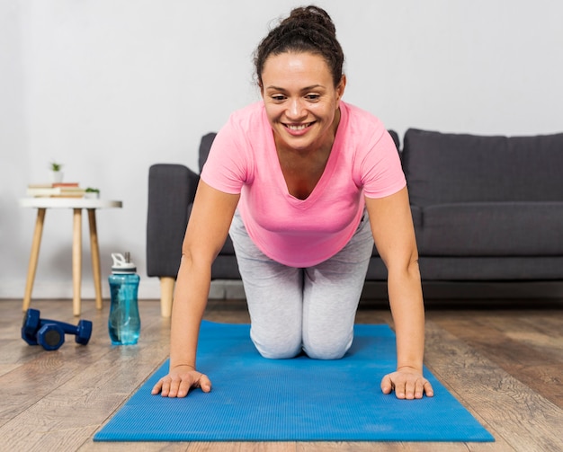 Smiley femme enceinte exercice sur tapis avec poids et bouteille d'eau