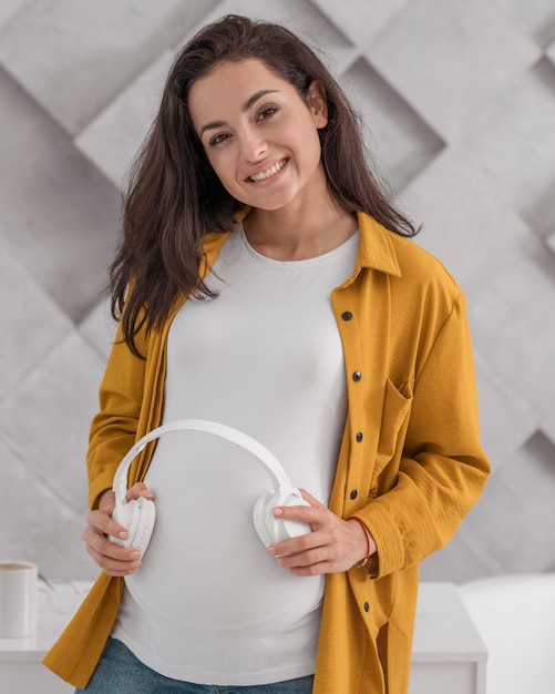 Smiley femme enceinte tenant des écouteurs sur son ventre